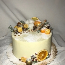 Торт на Рождество, покрыт кремом, декорированный дольками апельсина, палочками корицы белоснежным хлопком.